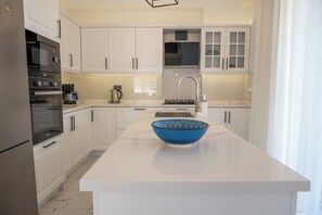 A modern kitchen with white cabinetry, a built-in oven, a coffee maker, and a blue bowl on the island.