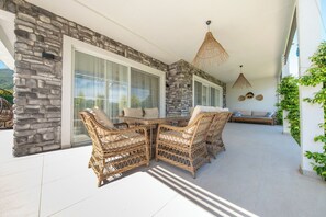 A covered patio with wicker furniture, stone walls, and large windows.