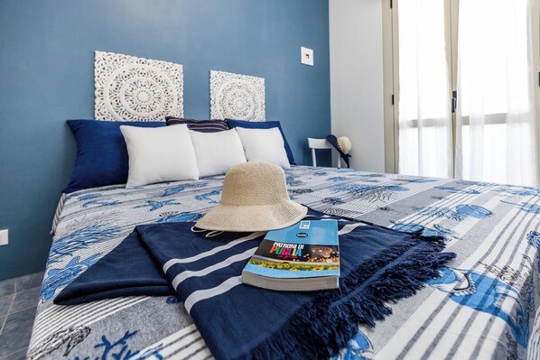 A neatly made bed with a blue and white patterned bedspread, a straw hat, and a book titled "Padrone di Puglia" on the bed.