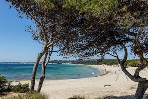 A beach with clear turquoise water, sandy shore, and a few people in the distance.