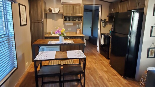 A compact kitchen with wooden cabinets, a black refrigerator, and a dining table with placemats. - Peaceful getaway for 2, dog friendly (Concho)