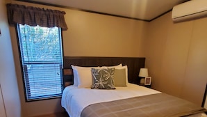 A bedroom with a bed, a window with blinds, a nightstand with a lamp, and an air conditioning unit. - Peaceful getaway for 2, dog friendly (Concho)