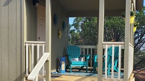 A covered porch with a wooden staircase leading up to a seating area with blue chairs and a table. - Peaceful getaway for 2, dog friendly (Concho)