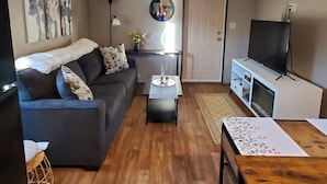 A living room with a sofa, coffee table, TV, and artwork on the wall. - Peaceful getaway for 2, dog friendly (Concho)