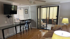 A living room with a flat-screen TV, a glass-top dining table with two chairs, a sofa, and a lamp. - Golfers getaway with sunny beaches too  (North Fort Myers)