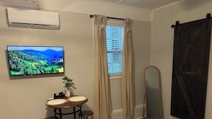 A room with a TV displaying a landscape, a small table with stools, a potted plant, and a sliding barn door. - Modern And Spacious Studio Retreat (Raleigh)
