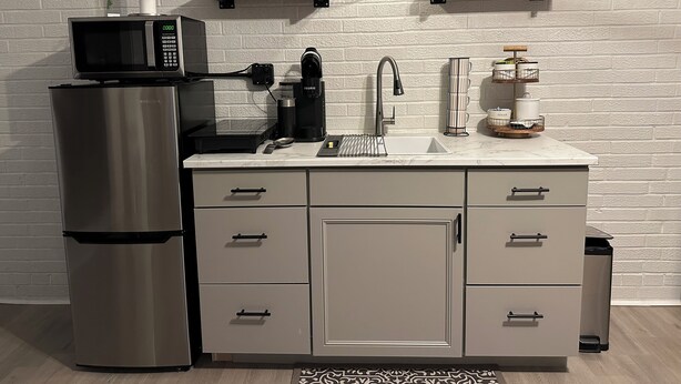 A modern kitchen with a stainless steel refrigerator, a microwave, a coffee maker, and a sink. There are cabinets and a trash bin. - Modern And Spacious Studio Retreat (Raleigh)