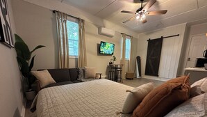 A bedroom with a large bed, a ceiling fan, a TV, and a sliding door. - Modern And Spacious Studio Retreat (Raleigh)