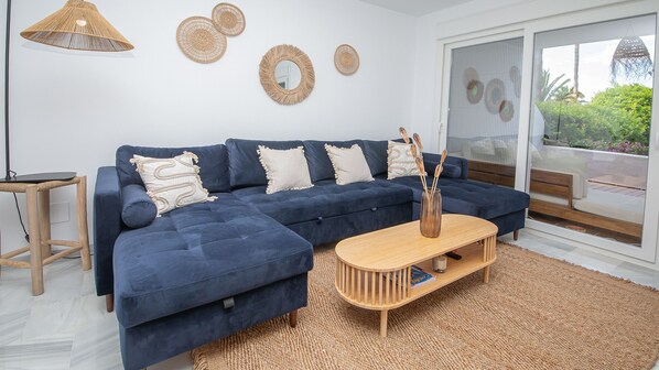 A modern living room with a dark blue sectional sofa, a wooden coffee table, and a woven rug. - Jardines de la Duquesa 26 (Manilva)