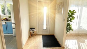 A hallway with a wooden floor, a black mat, a woven ceiling light fixture, and a door with a bright light. - VILLA EDOUARD - 180m2 in the heart of nature - 20min Disney - 7min Airport (Claye-Souilly)