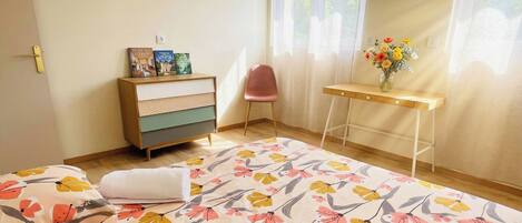 Un dormitorio con cama, cómoda, silla, escritorio y ventana con cortinas.