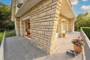 Une maison avec une façade en pierre, un porche couvert et un pot de fleurs.