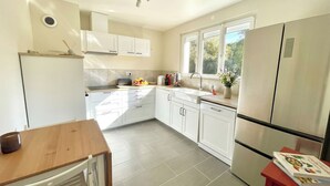 A modern kitchen with white cabinetry, a wooden table, and a window providing natural light. - VILLA EDOUARD - 180m2 in the heart of nature - 20min Disney - 7min Airport (Claye-Souilly)
