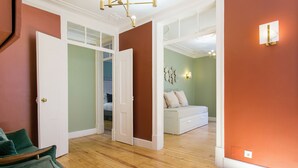 Une pièce avec un plancher en bois, un canapé vert et un lit blanc à l’arrière-plan.