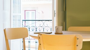 Une chaise et une table en bois, avec un téléphone intelligent et une tasse posés dessus, près d’une fenêtre donnant sur un balcon.