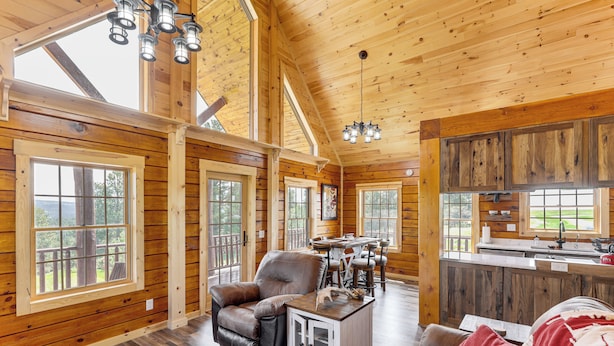 A spacious cabin with wooden walls and floors, large windows, a dining area, and a kitchen. - Peaceful Wyoming Cabin w/ Spacious Deck & Wet Bar! (Sundance)