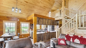 A spacious cabin interior with a wooden interior, a dining area, a kitchen, and a staircase leading to an upper level. - Peaceful Wyoming Cabin w/ Spacious Deck & Wet Bar! (Sundance)