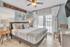 Cozy retreat with a large bed, striped bedspread, and nautical-themed pillow, complete with a ceiling fan and comfortable seating area.