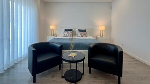 A modern hotel room with a large bed, two bedside tables with lamps, a small round table with a chair, and black leather armchairs. - Fantastic holiday home with heated pool (azeitão)