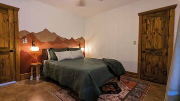 Een slaapkamer met een bed, een houten garderobe en een wanddecoratie met een berglandschap.