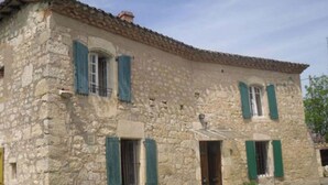 Edifici de pedra amb dues finestres, cadascuna amb persianes verdes, i una porta.