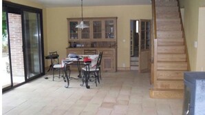 Una zona de menjador amb taula i cadires, una cuina amb armaris i una escala de fusta.