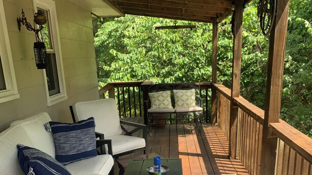A covered porch with a wooden deck, a white sofa with blue cushions, a small table with a water bottle, and a patterned rug. - Whitley Woods Cottage, secluded on 80 acres, Chadwick MO (Chadwick)