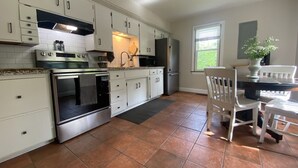 A modern kitchen with white cabinets, stainless steel appliances, and a dining area with a table and chairs. - Whitley Woods Cottage, secluded on 80 acres, Chadwick MO (Chadwick)