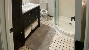 A bathroom with a dark wooden vanity, white sink, and toilet. There is a glass-enclosed shower area with a white bathtub. - Whitley Woods Cottage, secluded on 80 acres, Chadwick MO (Chadwick)