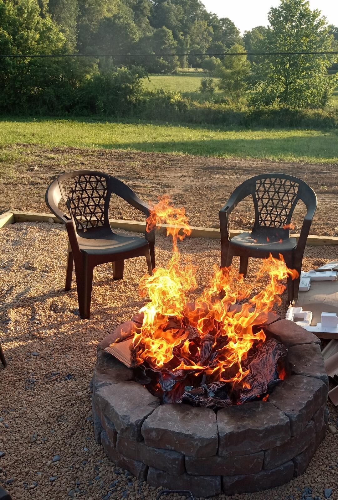 A fire pit with burning logs surrounded by two chairs.