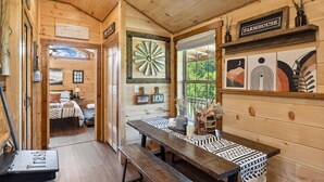 A rustic wooden interior with a dining table, benches, and a wall clock.