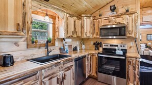 A rustic kitchen with wooden cabinetry, a stainless steel microwave, an oven, and a sink.