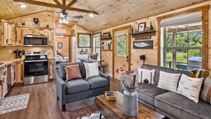 A cozy cabin interior with wooden walls, a dining area, a kitchen with modern appliances, and a comfortable seating area with a fireplace.