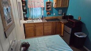 A compact kitchen with wooden cabinets, a sink, a microwave, and a small trash bin.