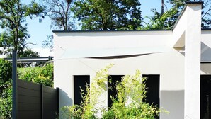 A modern building with a white exterior, a black planter with green plants, and a gravel ground. - Villa Romantique (ANDANCETTE)