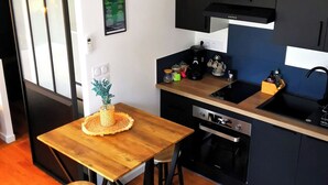 A compact kitchen with a wooden dining table, a built-in oven, and a black countertop. - Villa Romantique (ANDANCETTE)