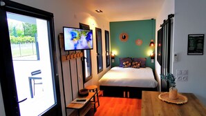 A compact hotel room with a bed, a desk, a TV, and a view of the outdoors. - Villa Romantique (ANDANCETTE)
