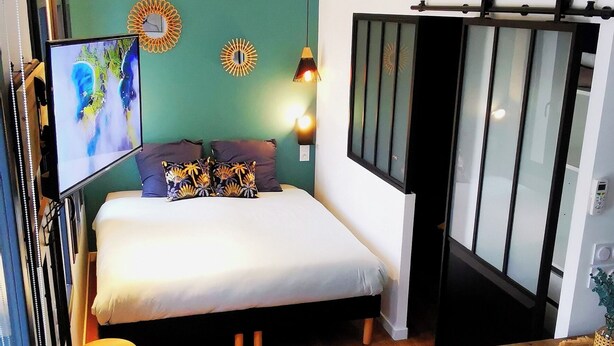 A compact hotel room with a bed, a small table, a chair, and a TV. - Villa Romantique (ANDANCETTE)