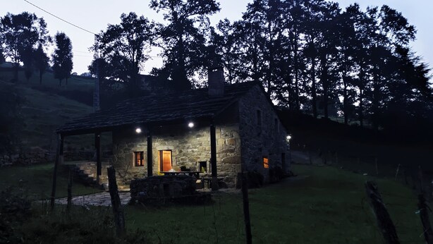 Un cottage in pietra con un portico, un camino e un tavolino con sedie all'esterno.