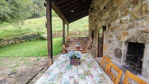 Un'area pranzo all'aperto coperta con parete in pietra, tavolo in legno con tovaglia floreale e camino in pietra.