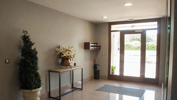 A clean, modern lobby with a reception desk, a potted plant, and a glass door leading outside. - Apartamento Sorkun (Lakuntza)