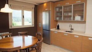 A modern kitchen with wooden cabinets, a stainless steel refrigerator, a dining table with chairs, and a window with a view of greenery. - Apartamento Sorkun (Lakuntza)