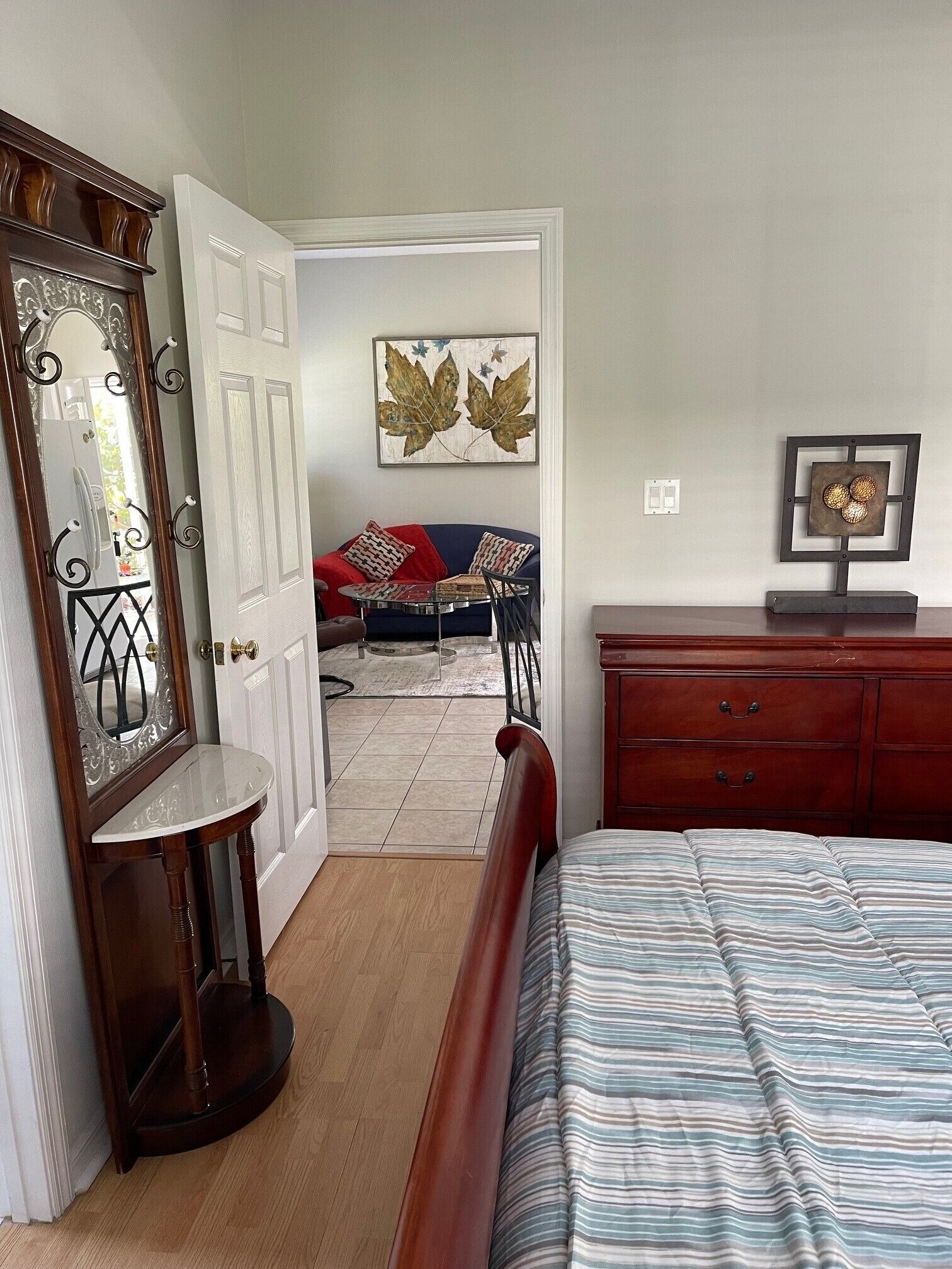 A bedroom with a bed, dresser, mirror, and artwork on the wall.