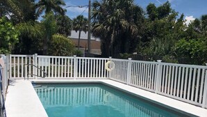 A rectangular swimming pool with a white fence surrounding it, a lounge chair, and a palm tree in the background. - Walk to Siesta Key Beach. 1 BR condo on ground floor, steps away from the pool (Sarasota)