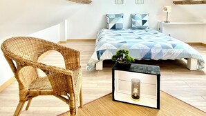 A bedroom with a sloped ceiling, a bed with a geometric patterned duvet, a wicker chair, a small table with a plant, and a skylight. - Beau Duplex à Deux pas du Port (Le Tréport)