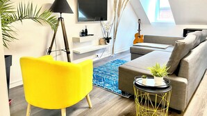 A modern living room with a sofa, a yellow chair, a TV, a guitar, and a plant. - Beau Duplex à Deux pas du Port (Le Tréport)