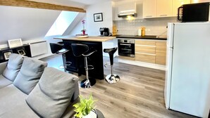 A modern kitchen with a central island, a dining area with a sofa, and a refrigerator. - Beau Duplex à Deux pas du Port (Le Tréport)