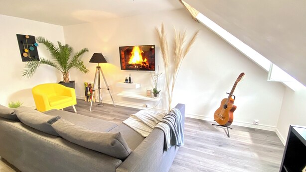 A modern living room with a grey sofa, a yellow armchair, a mounted TV, a guitar, and a tripod lamp. - Beau Duplex à Deux pas du Port (Le Tréport)