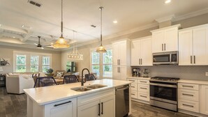 A spacious kitchen with white cabinets, a large island with a sink, stainless steel appliances, and pendant lighting.