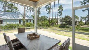 A covered patio with a table and chairs, overlooking a residential area with houses and tall trees.